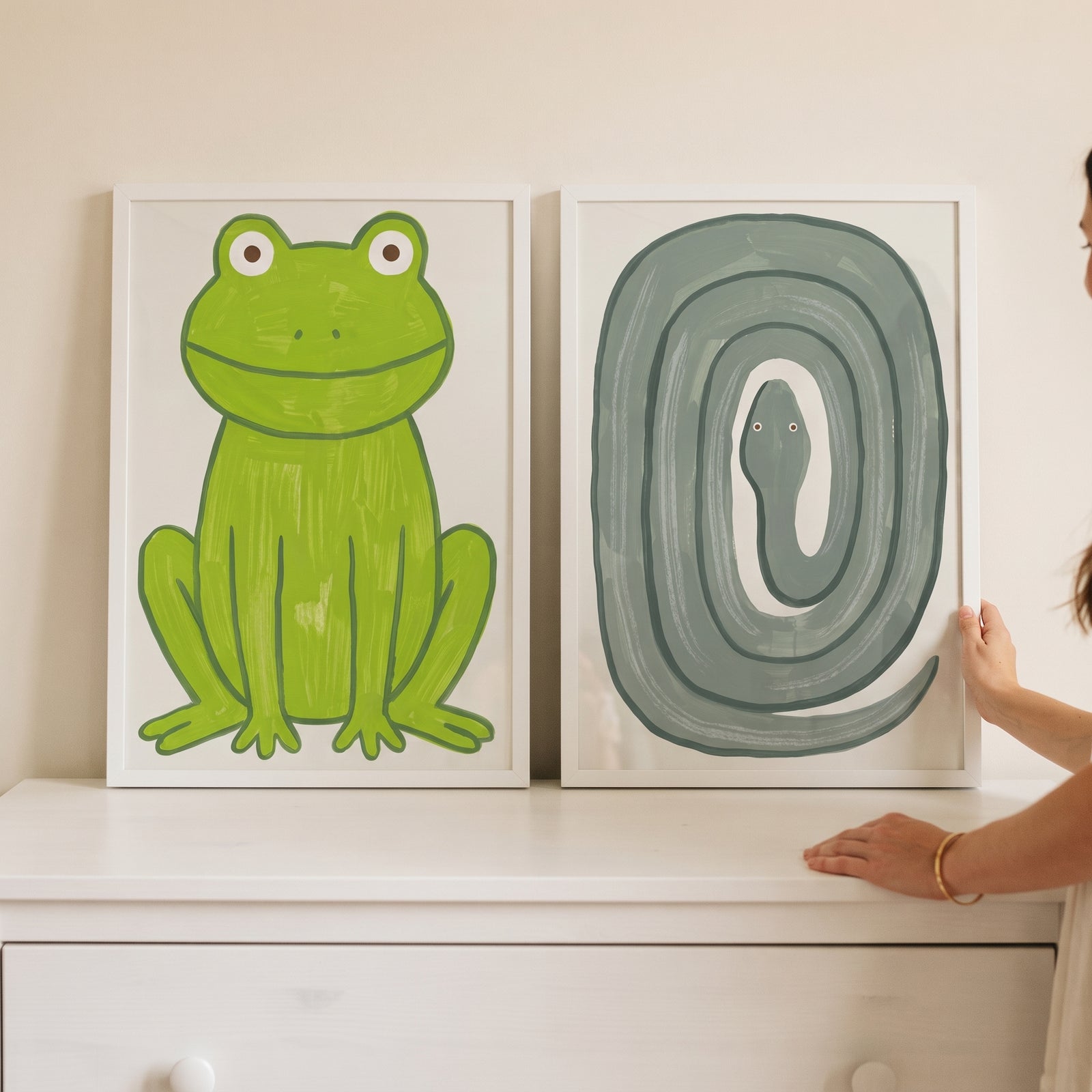 Minimalist brushstroke green animals wall art set of 2 featuring a frog and a coiled snake on a white dresser.