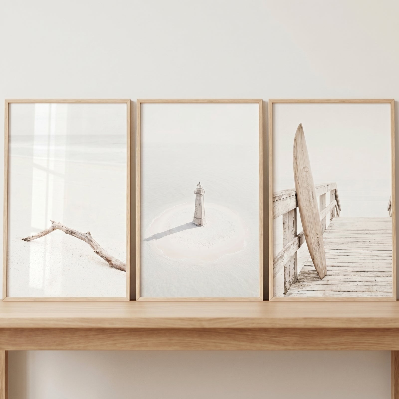 Minimalist neutral landscape coastal wall art set of 3 featuring driftwood, a lighthouse, and a surfboard on a pier.