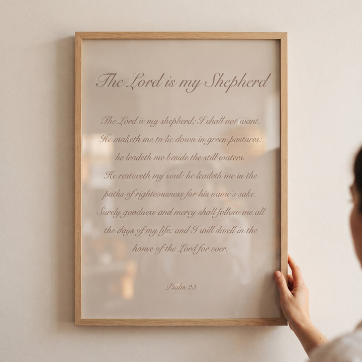 Minimalist neutral psalm 23 wall art in a light wood frame held by a person against a beige wall.