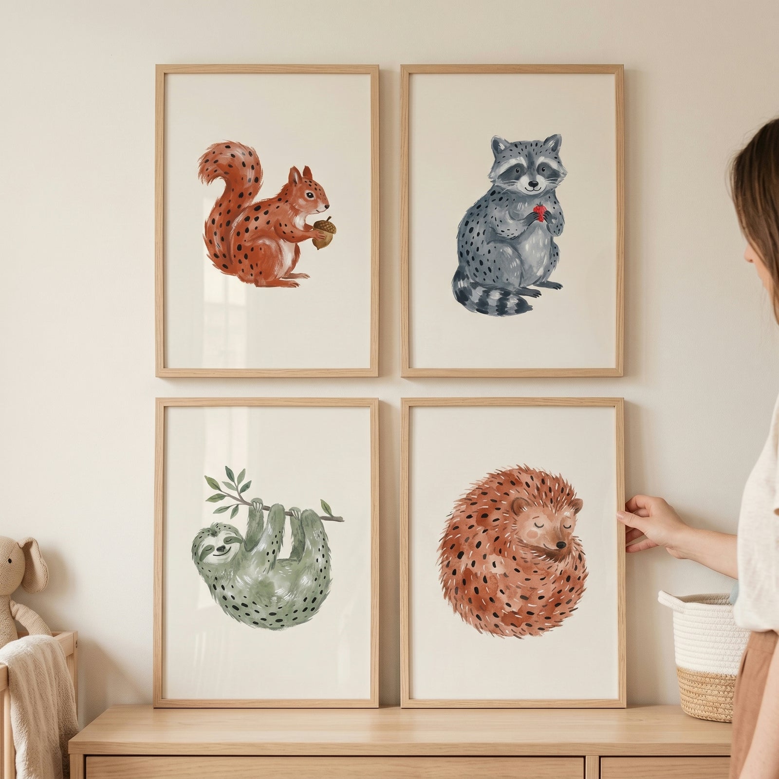 A hand adjusts a minimalist neutral woodland animals wall art set of 4 featuring a squirrel, raccoon, sloth, and hedgehog.