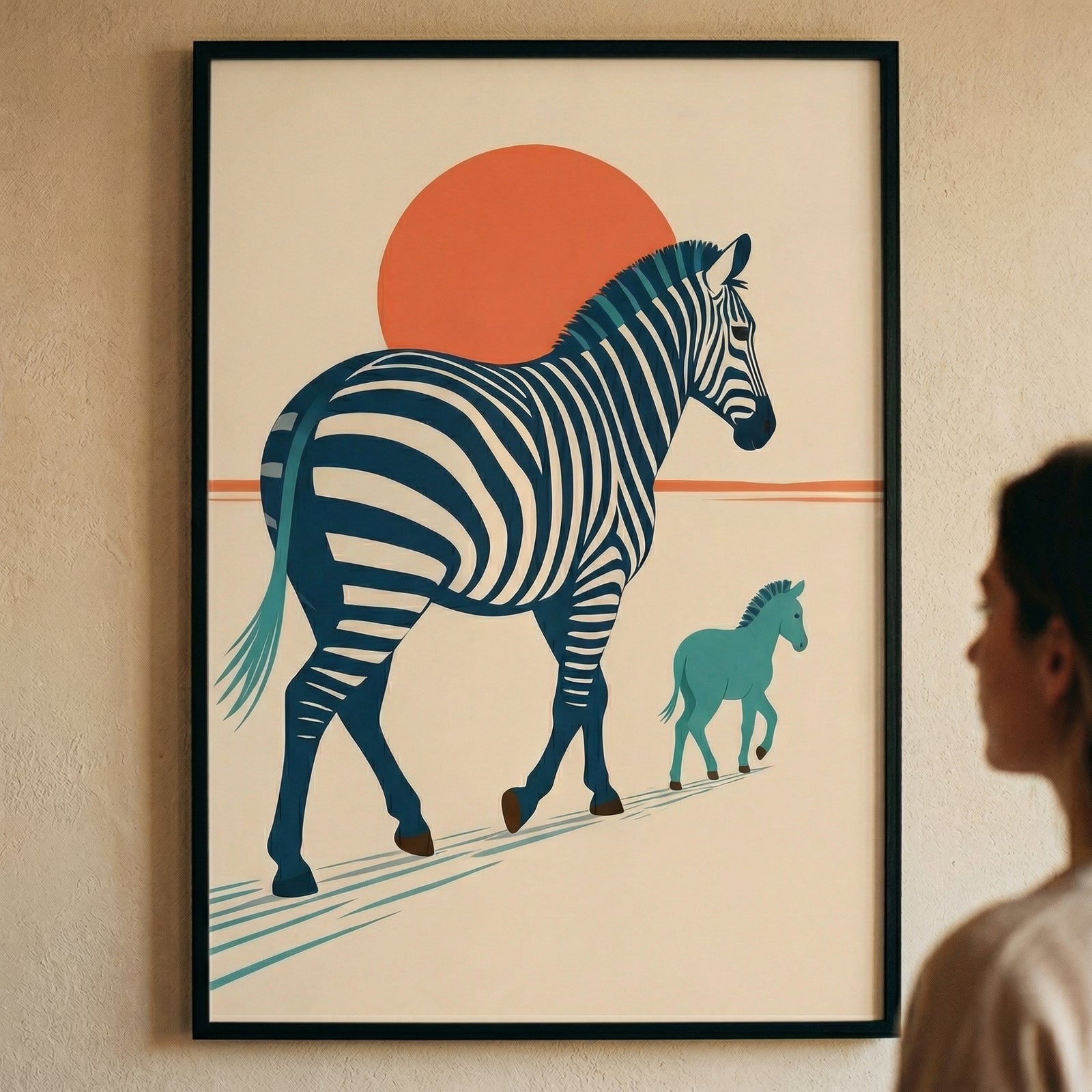 A piece of graphic art is displayed in a black frame on a light, textured wall. The artwork depicts a large zebra with bold dark blue and white stripes. Behind the zebra's back is a large, solid orange circle resembling a sun. A smaller, solid teal young equine figure follows closely behind. The scene is set against an off-white background with minimalist lines indicating the ground. In the foreground, the side of a person's head and shoulder are visible as they look toward the wall-mounted art.