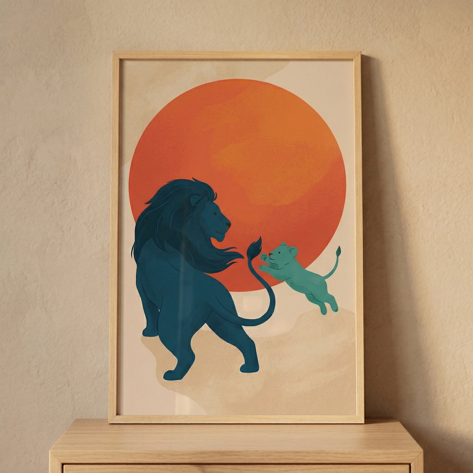 Framed illustration of a blue lion with flowing mane turning toward a playful cub mid leap in front of a large warm red sun. The artwork creates a cheerful focal point above a dresser adding a sense of movement and warmth to a nursery space.