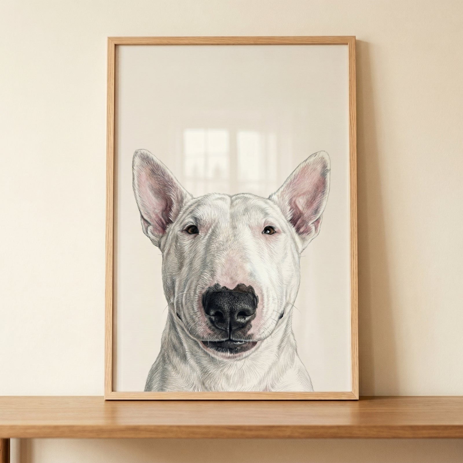 Minimalist white bull terrier wall art in a wooden frame rests on a table against a light beige wall.