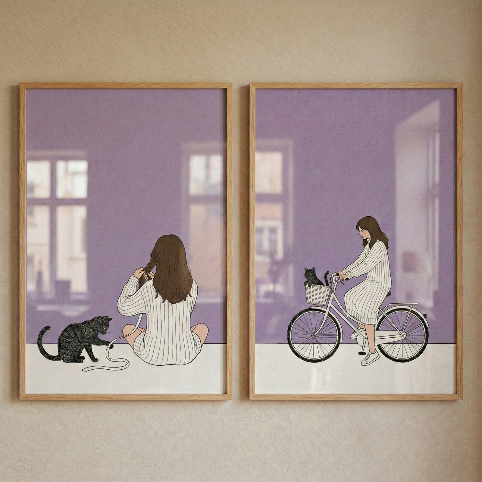 Two framed illustrations with thin wooden frames hang side-by-side on a light beige wall. Each features a minimalist style with a soft purple background and a white foreground. The left illustration shows a woman from behind, sitting on the floor in an oversized white striped sweater, holding a long ribbon. A dark tabby cat sits beside her, batting at the ribbon. In the right illustration, the woman rides a white bicycle, with the same cat sitting in the front basket.
