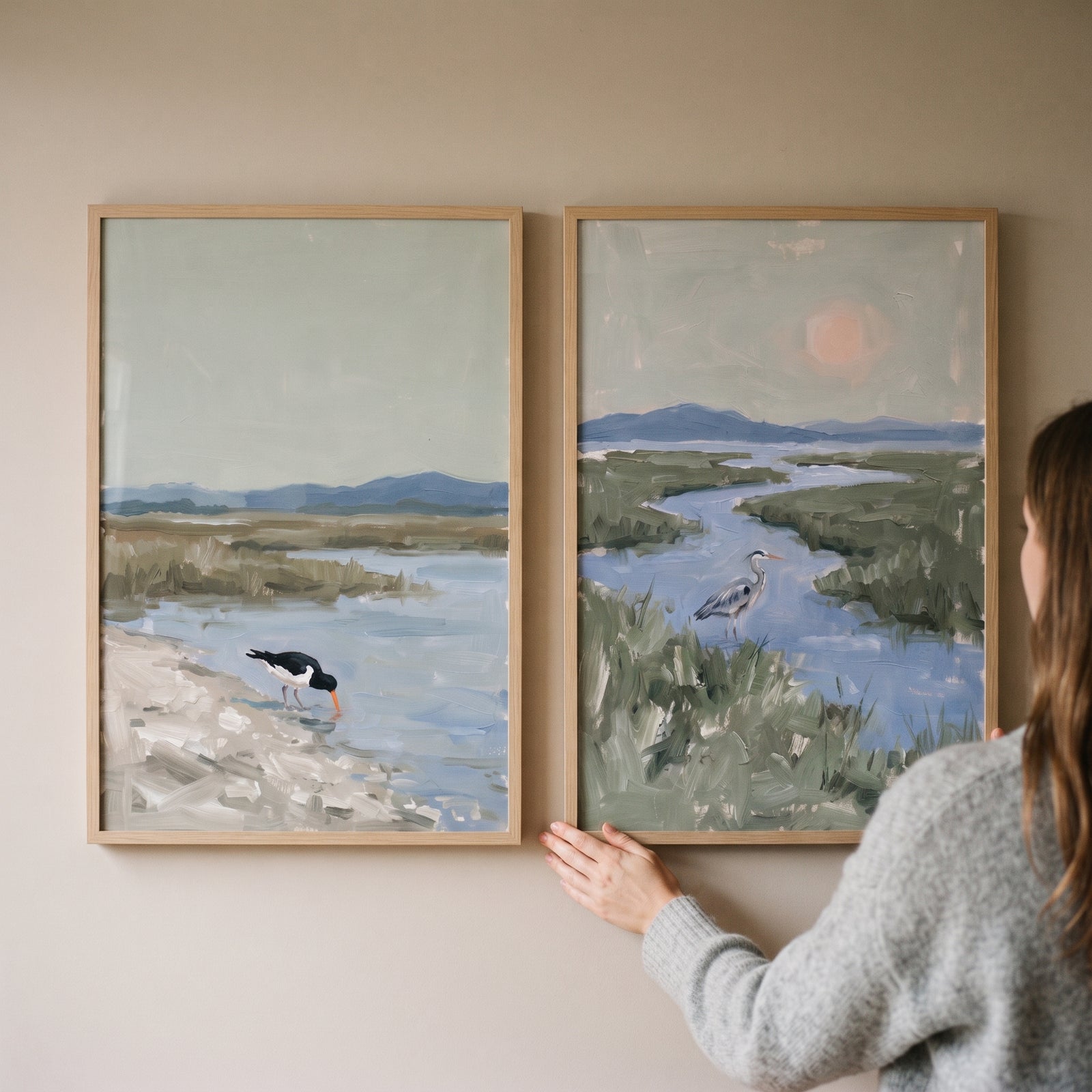 A person hangs a misty sage wetland bird wall art set of 2 featuring hazy marshland scenes and shorebirds.