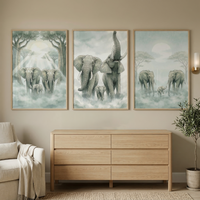 "A serene room interior features a set of three framed vertical artworks displayed on a neutral-toned wall. The illustrations depict a family of elephants in various soft, misty landscapes. The first piece shows three elephants emerging from a sun-dappled forest with light rays filtering through the trees. The second piece captures two large elephants and a calf under a cloudy sky, with one adult elephant triumphantly raising its trunk.