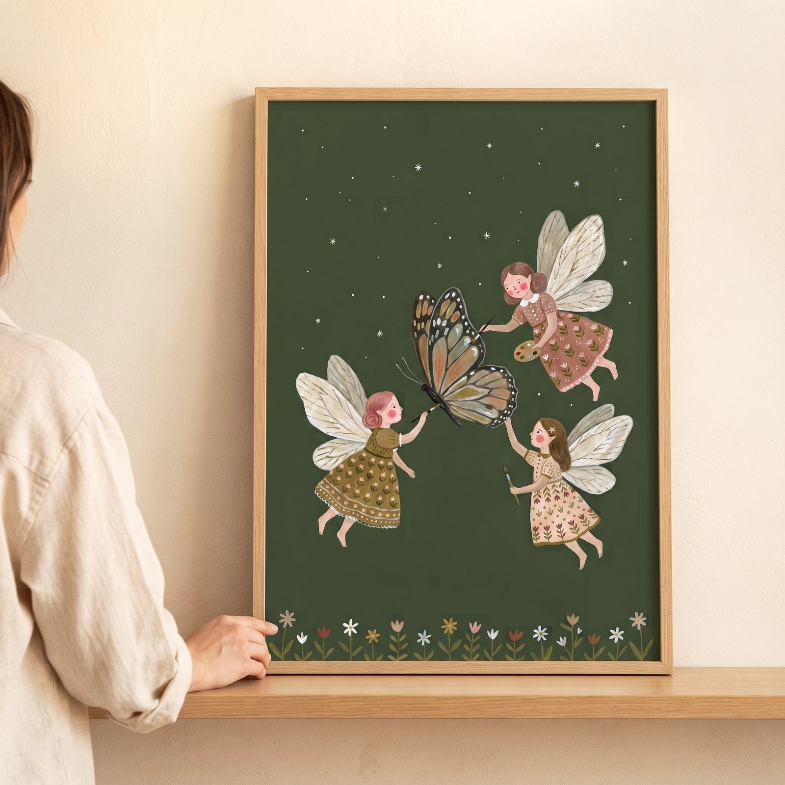 Monarch butterfly artist fairies wall art shows three winged figures decorating a butterfly against a starry green sky.
