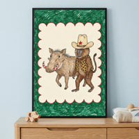 Framed illustration of a baboon wearing a cowboy hat and leopard vest with its arm around a smiling warthog, displayed on a light wood dresser against a pale blue wall.