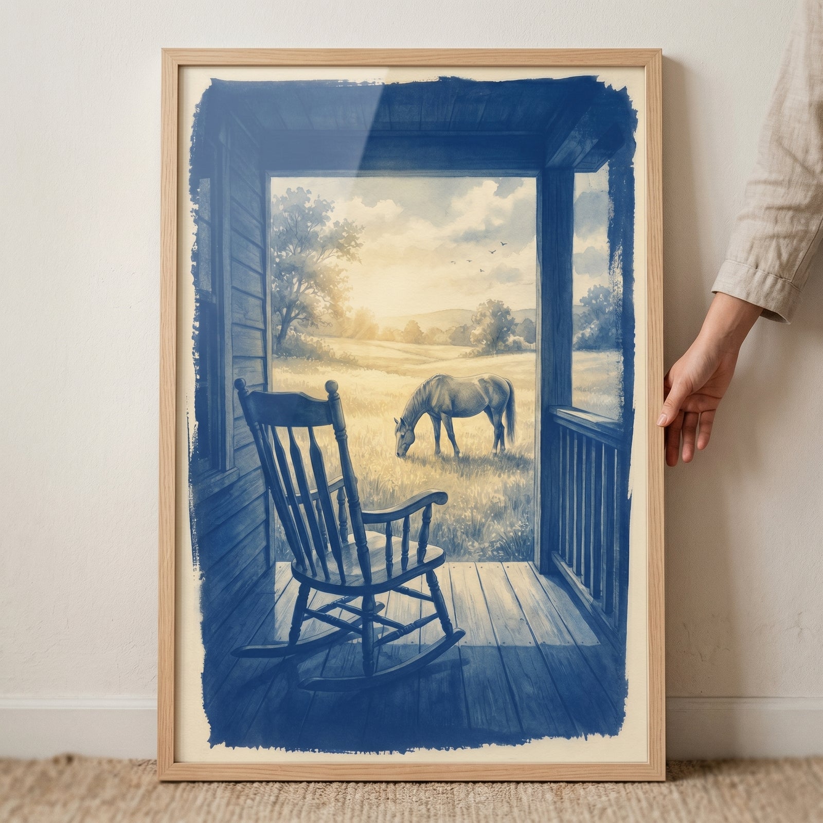 Monochrome blue grazing horse wall art depicts a rocking chair on a porch overlooking a horse in a sunlit field.