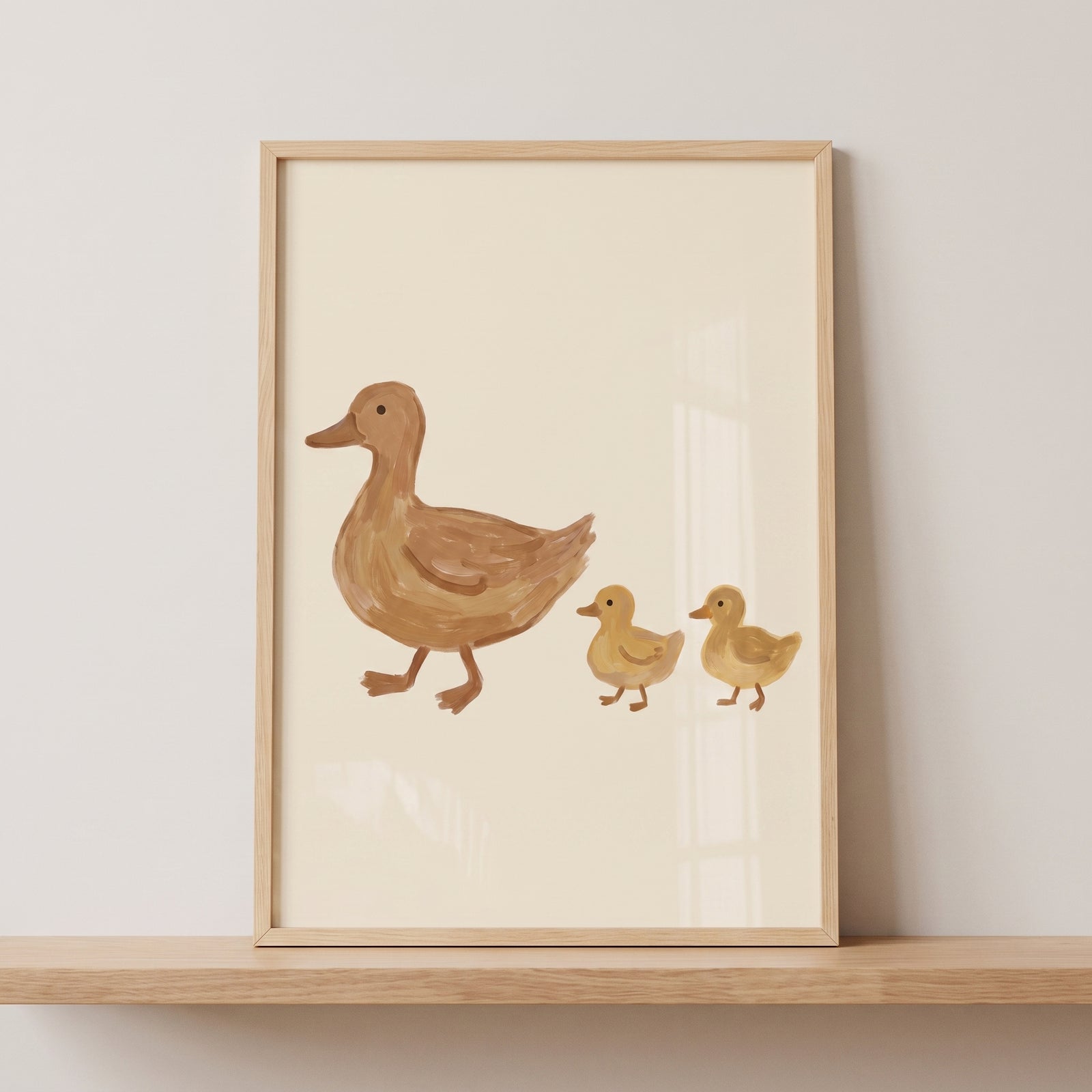 Mother and baby duck wall art in a wooden frame shows a brown duck followed by two yellow ducklings on a tan background.