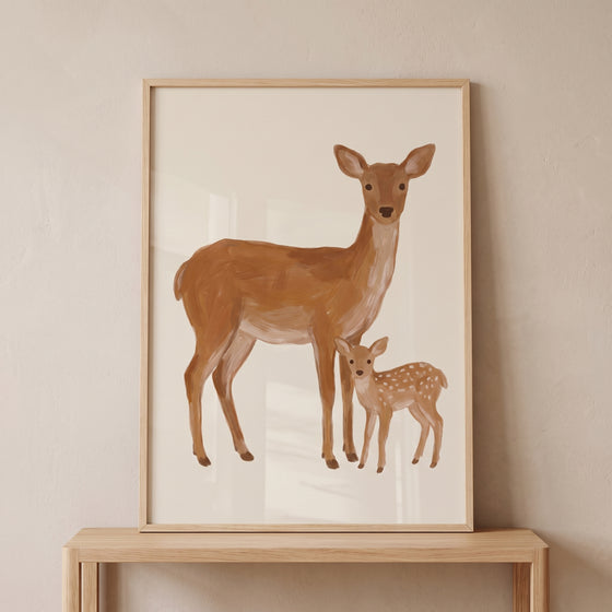 Mother baby deer wall art in a wooden frame on a console table, featuring a brown doe and spotted fawn against a beige wall.