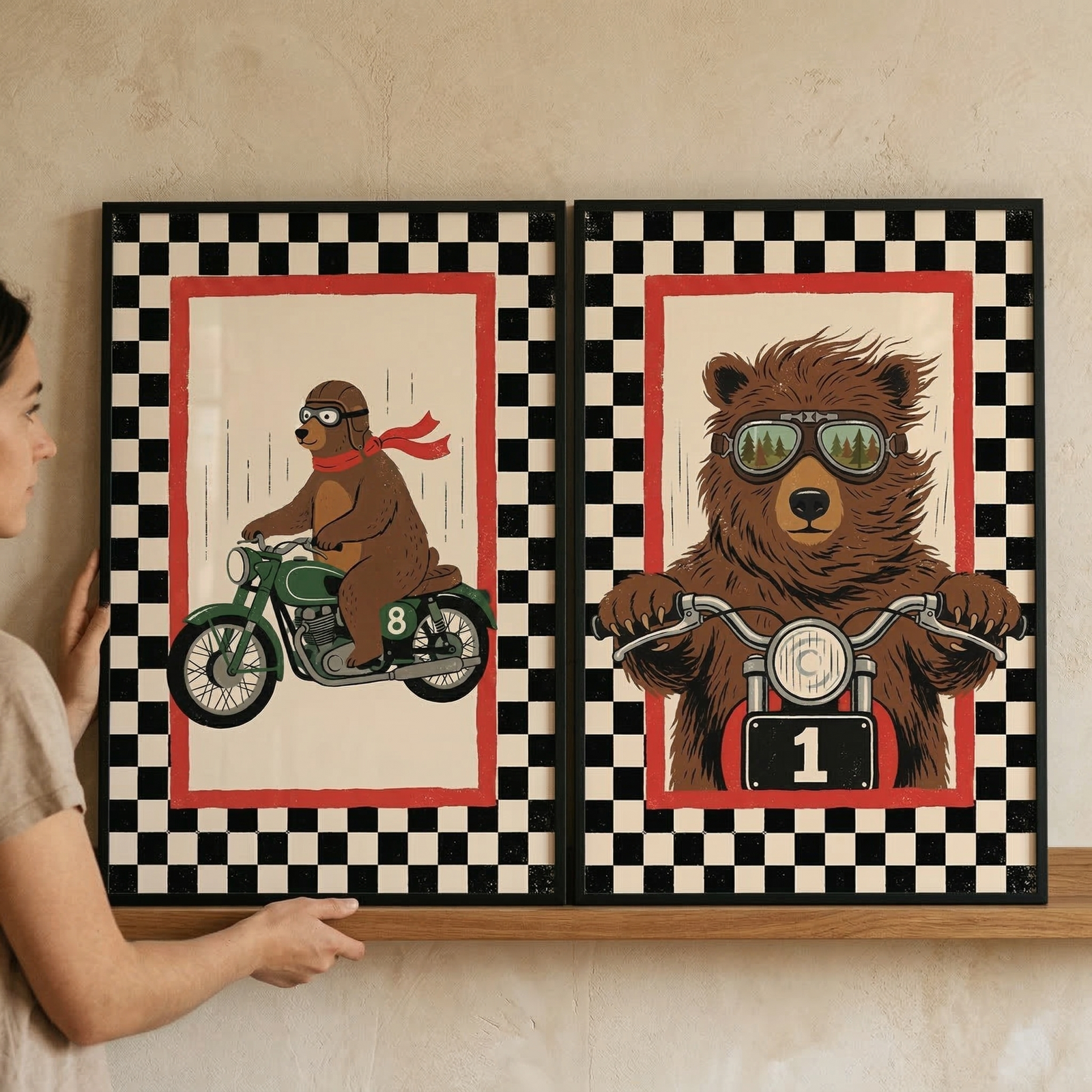 A person is seen from the side, holding two rectangular framed art prints onto a wooden shelf. The prints feature vintage-style illustrations of brown bears as motorcyclists.

The print on the left shows a profile view of a brown bear riding a green motorcycle. The bear is wearing a brown leather cap, goggles, and a long red scarf that flows behind it, suggesting movement. Small vertical lines in the background further enhance the sense of speed.