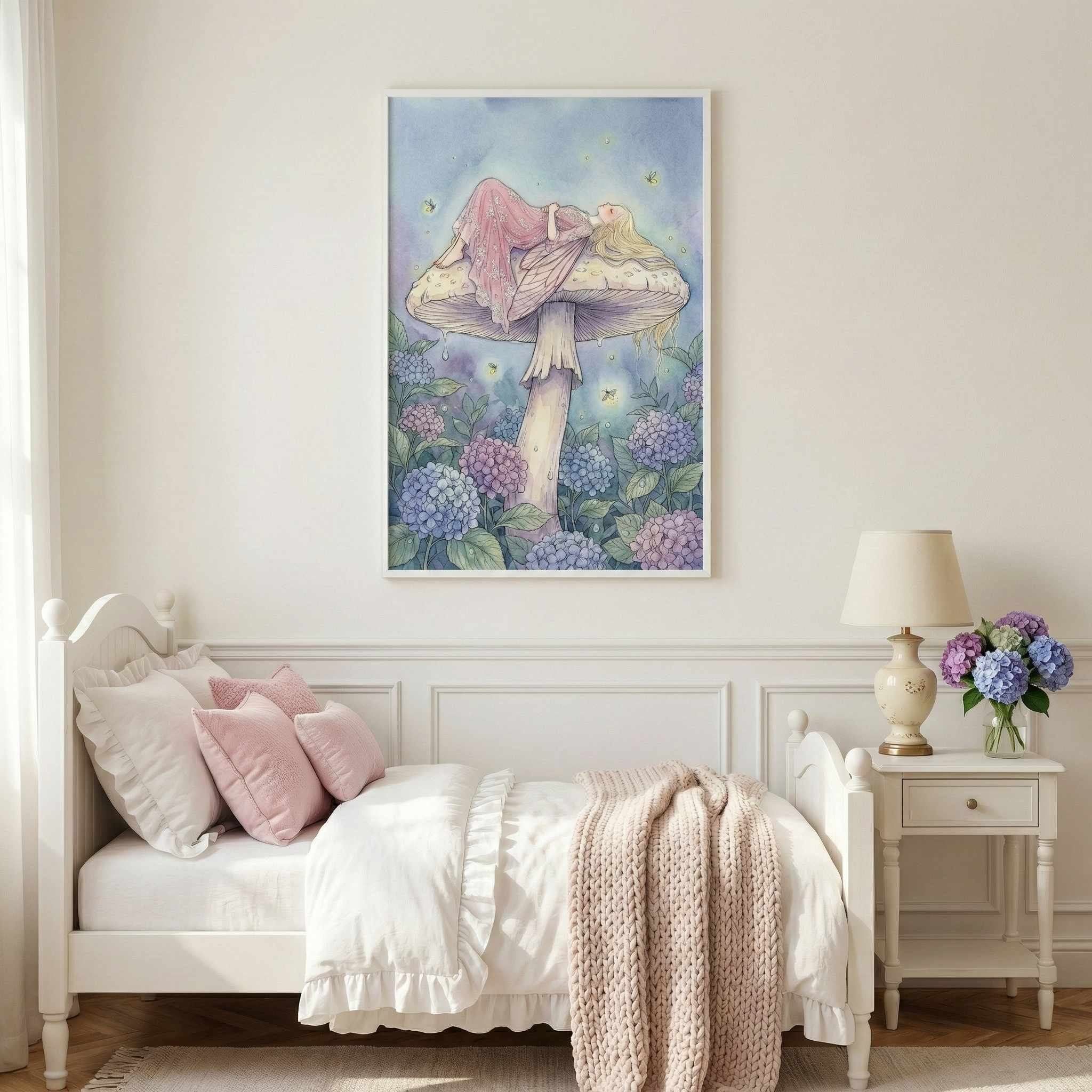 A cozy bedroom features a framed vertical illustration centered on an off-white wall. The artwork depicts a fairy with long blonde hair and a pink dress resting on top of a large, pale mushroom, surrounded by clusters of blue and purple hydrangeas. Below, a white wooden bed is dressed in white and pink linens. Beside the bed, a white nightstand holds a vintage-style lamp and a small bouquet of purple and blue hydrangeas, echoing the colors in the wall art.