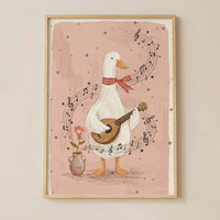 Framed illustration of a white duck wearing a red checkered scarf while playing a small guitar with musical notes swirling around it on a soft pink background. A small vase with a single flower sits beside the duck, adding to the whimsical and cozy nursery wall decor feel.