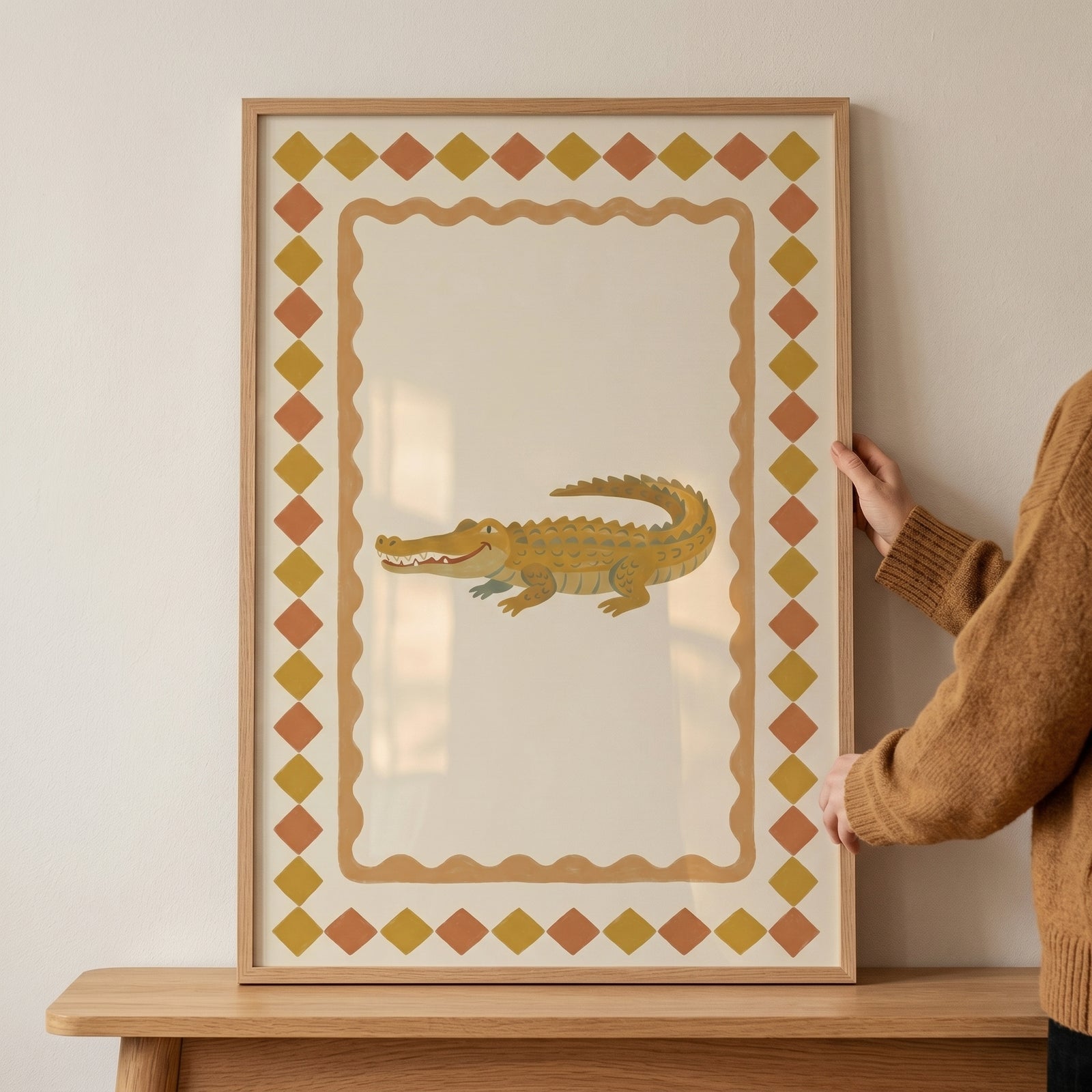 Mustard diamond border crocodile wall art in a light wood frame held by a person against a neutral wall.