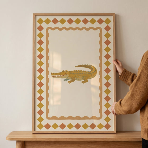 Mustard diamond border crocodile wall art in a light wood frame held by a person against a neutral wall.