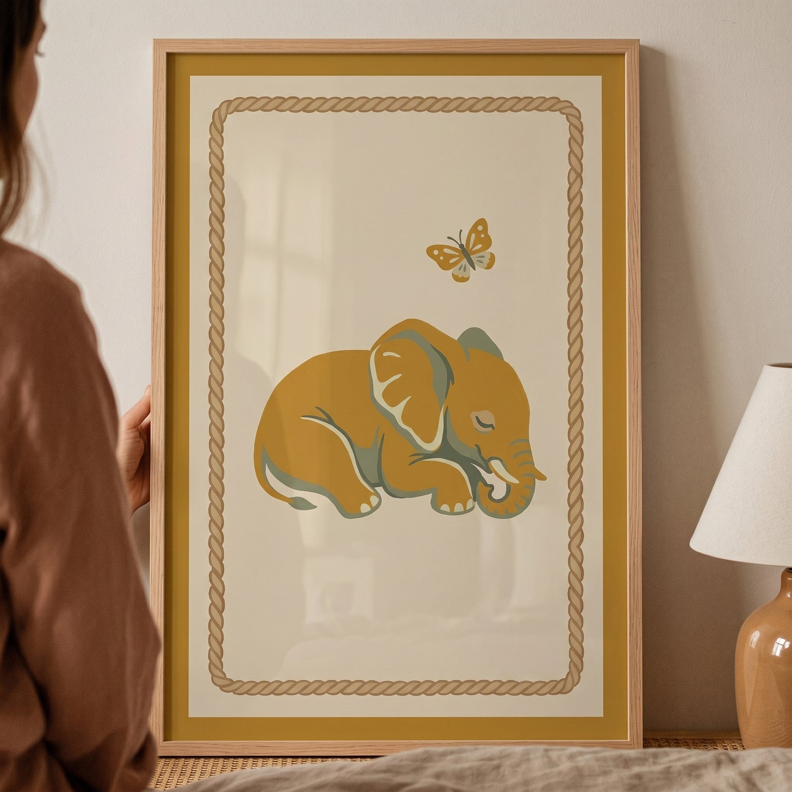 Mustard yellow sleeping elephant wall art with a butterfly and rope border inside a light wood frame.
