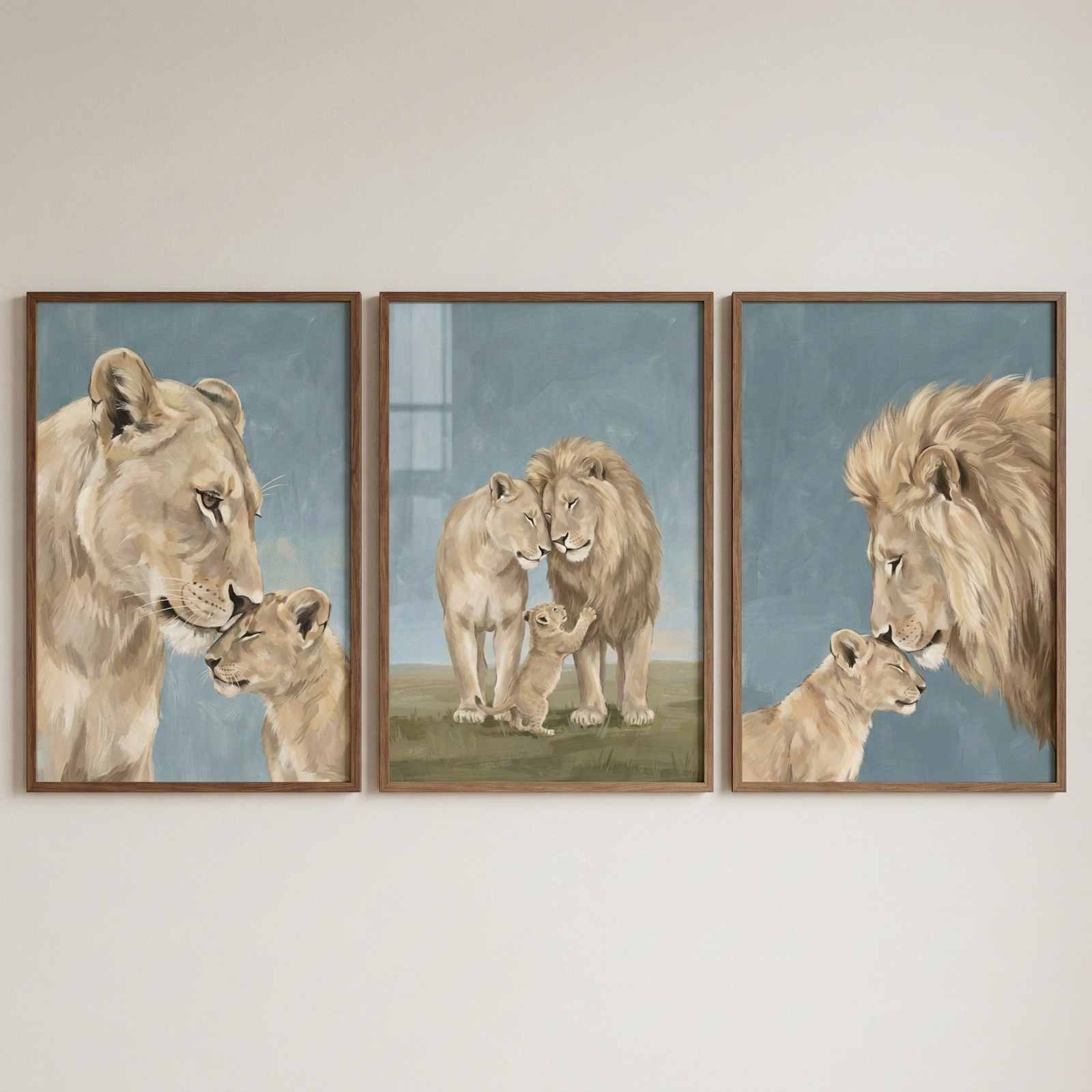 Three wooden-framed artworks hang side-by-side on a plain wall, each featuring gentle illustrations of a lion family. The left piece shows a lioness tenderly nuzzling a cub. The center piece depicts a lioness and a male lion with a full mane standing together while a small cub stands on its hind legs between them. The right piece shows the male lion nuzzling a cub. All three artworks have a soft, illustrative style with a muted blue-gray background.