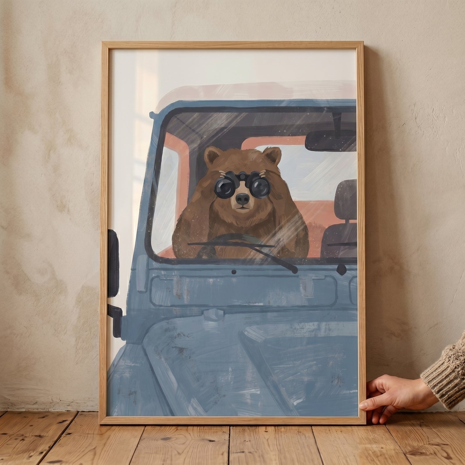 Brown bear peering through binoculars in this muted blue vehicle bear wall art displayed in a light wooden frame.