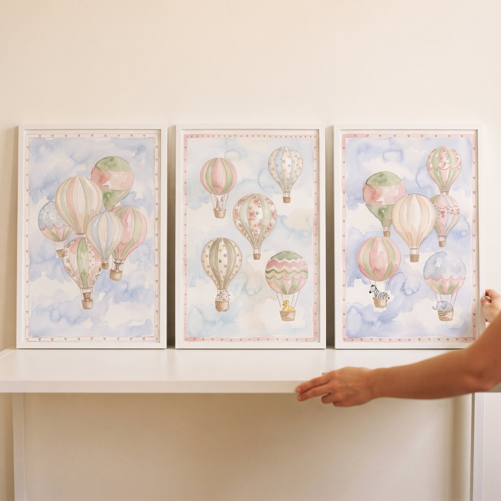 Muted hot air balloon wall art set of 3 features soft pastel balloons and animals in white frames on a white shelf.