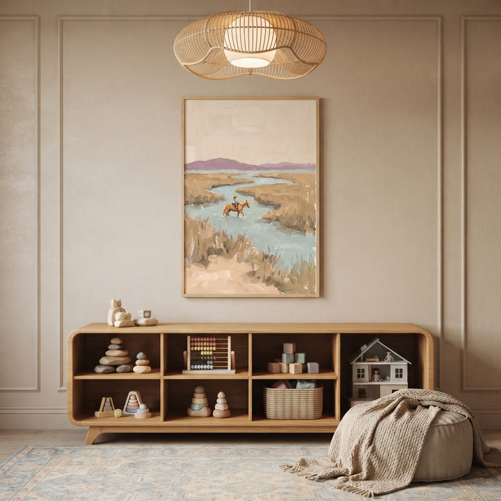 Muted landscape horse rider wall art hangs above a low wooden shelf in a neutral room with a woven light and soft rug.