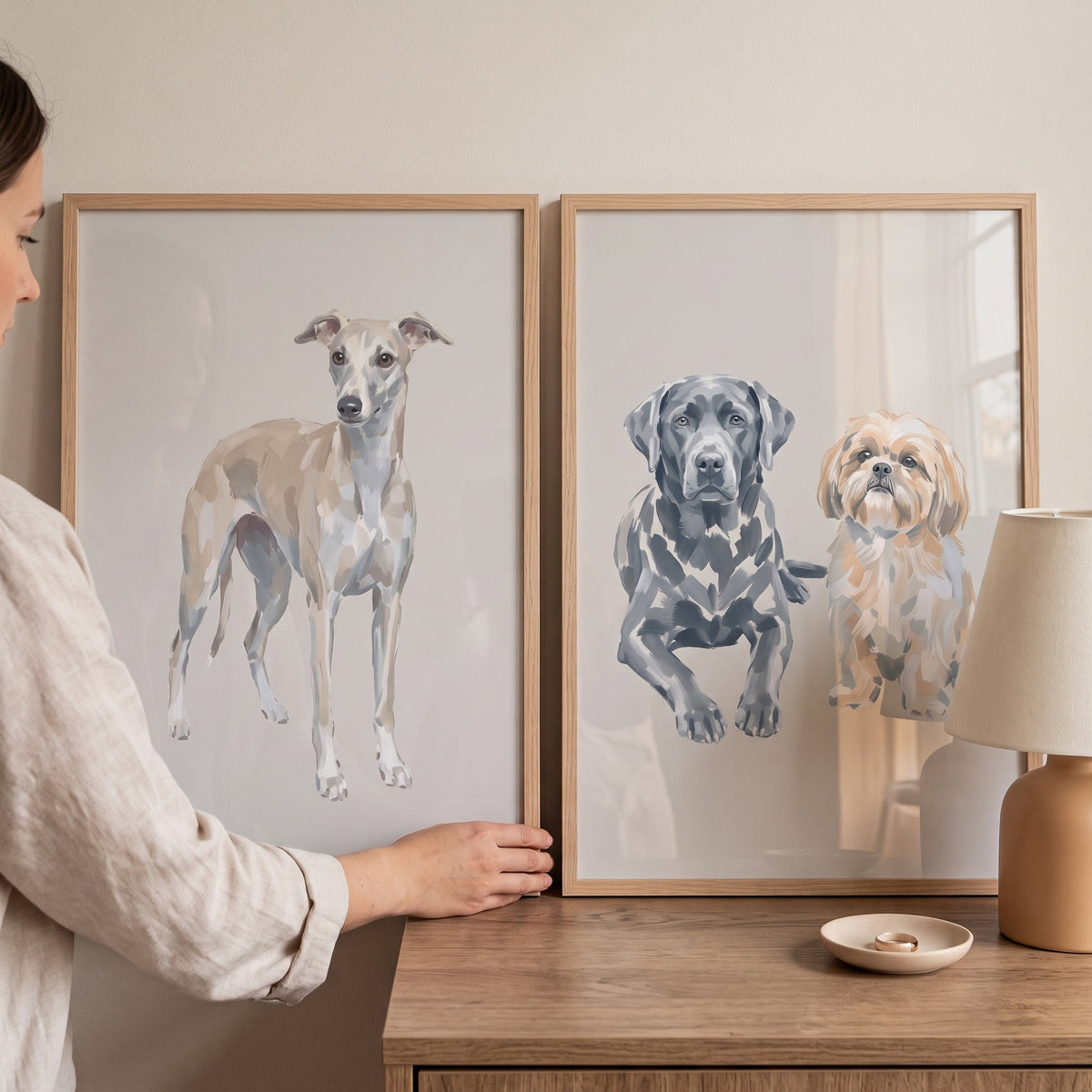 Woman's hands adjust a muted neutral beige dogs wall art set of 2 featuring three dog illustrations on a wooden surface.