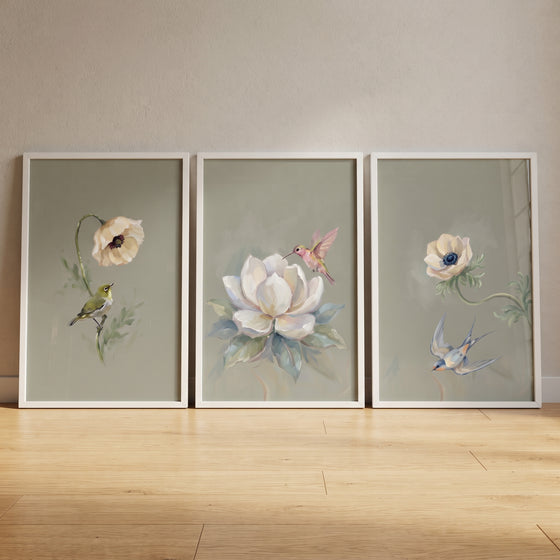 Muted palette garden bird artwork set of 3 displays birds and flowers in white frames on a wooden floor.