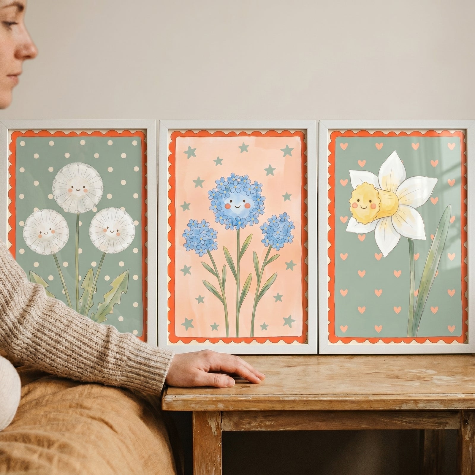 Muted pastel smiling flower wall art set of 3 with dandelions, blue flowers, and a daffodil in frames on a wooden table.