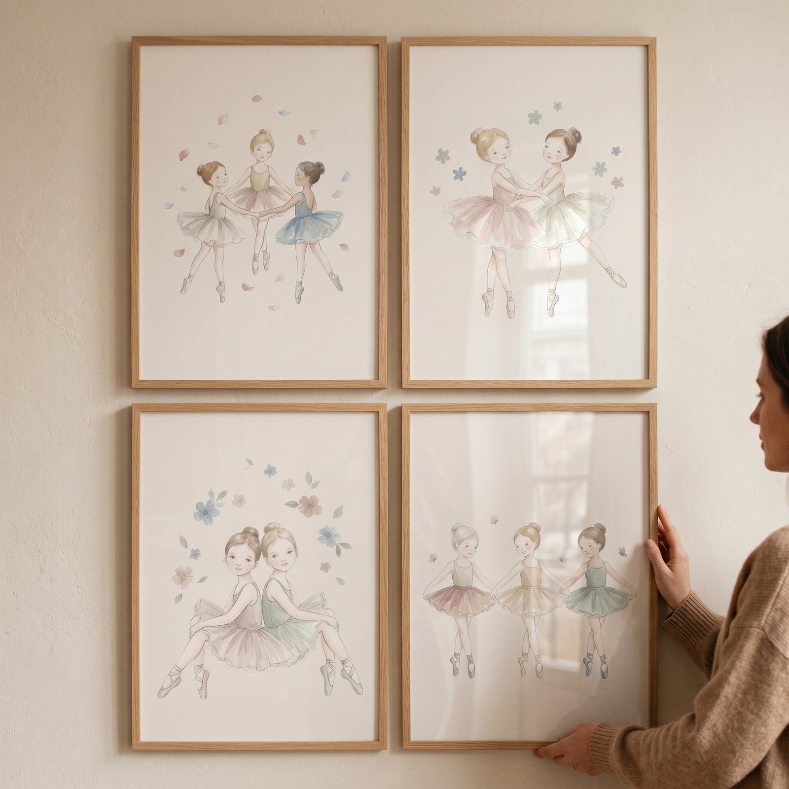 A woman adjusts a muted pastel watercolor ballerina wall art set of 4 framed illustrations hanging on a neutral wall.
