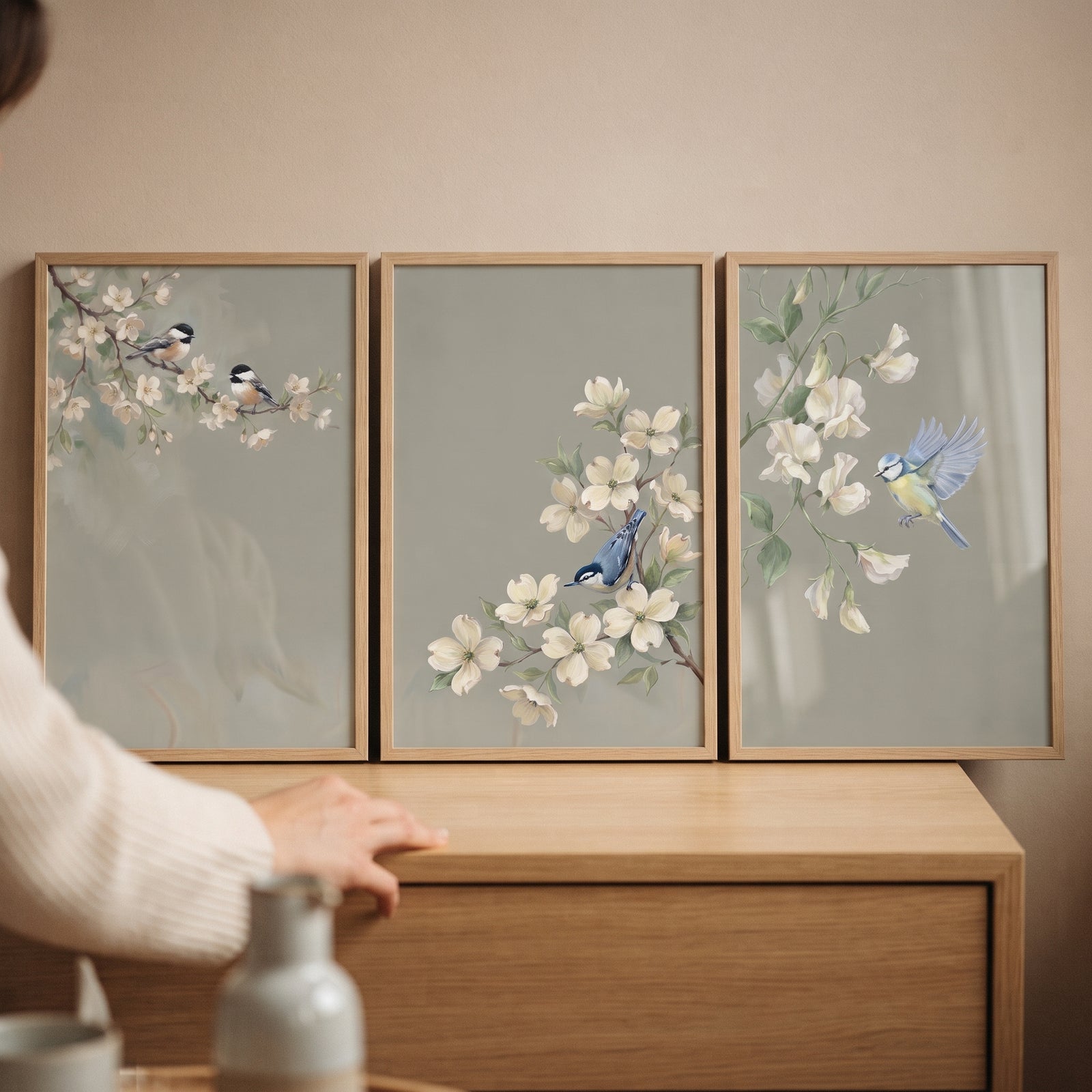 Muted sage botanical bird wall art set of 3 framed prints on a dresser featuring birds and white blossoms.