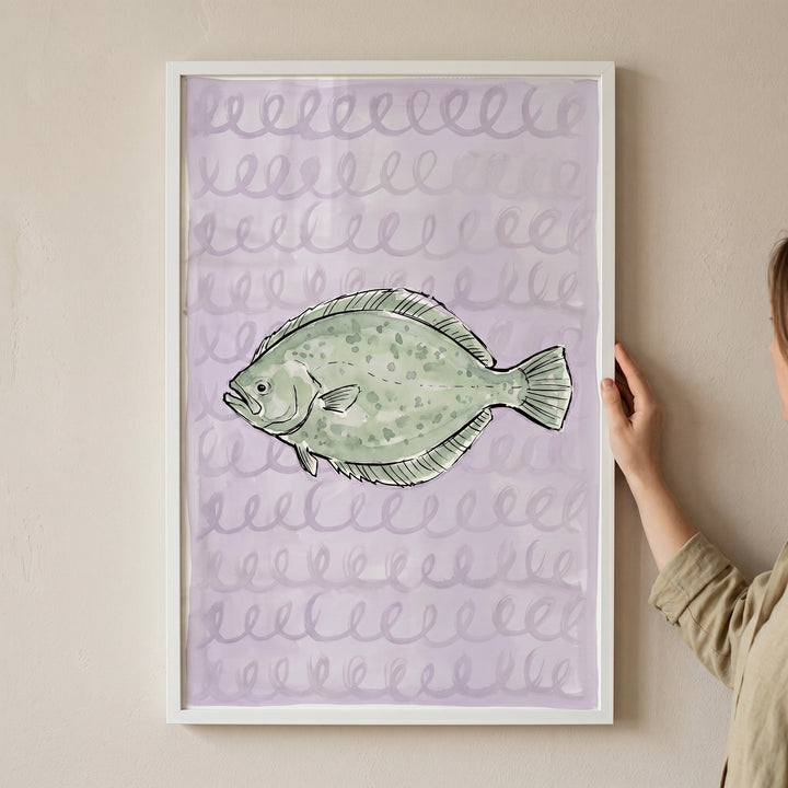 Muted sage green flatfish wall art in a white frame with purple swirls, held against a wall by a person.