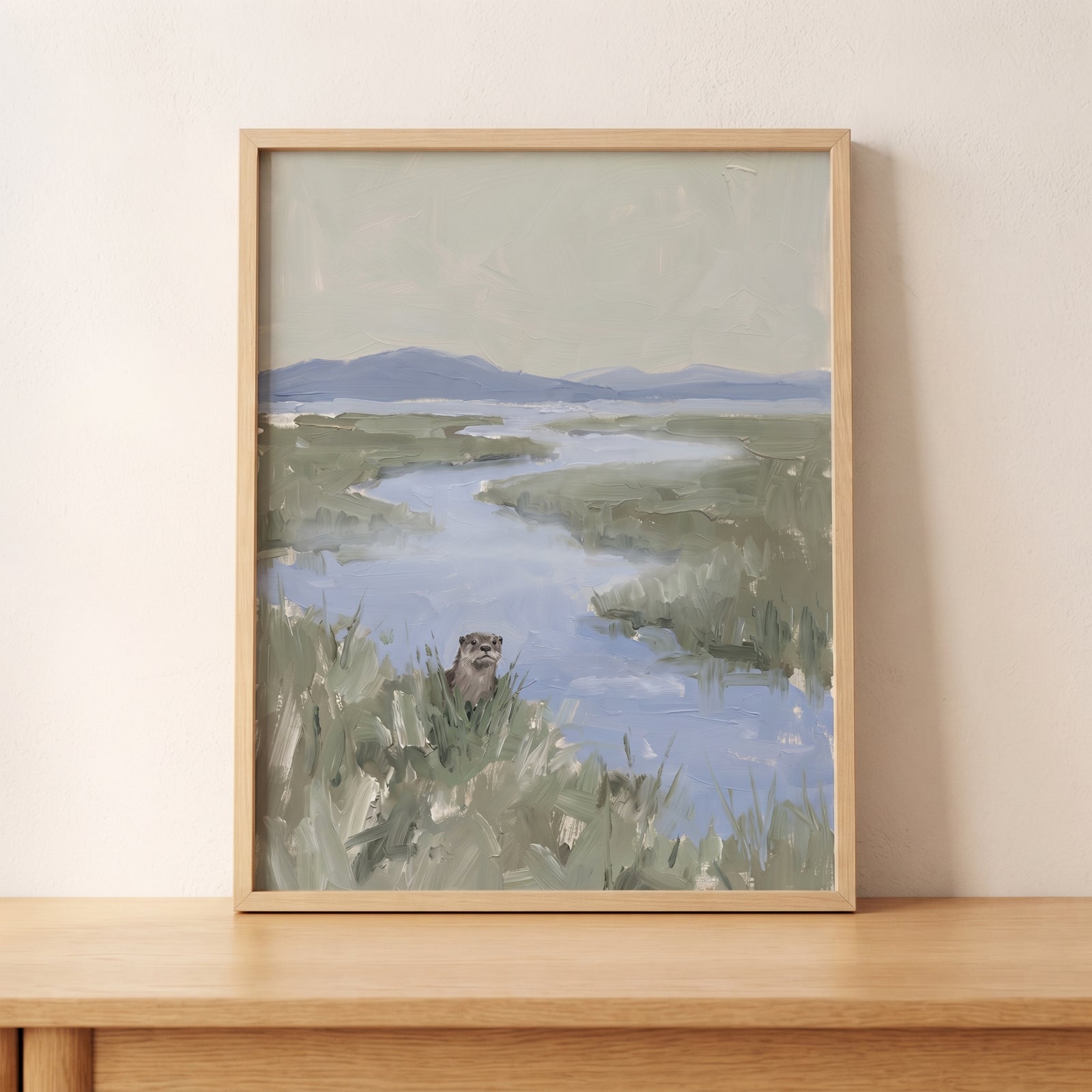 Muted sage green otter artwork of an otter in a marshy river landscape with distant mountains in a light wood frame.