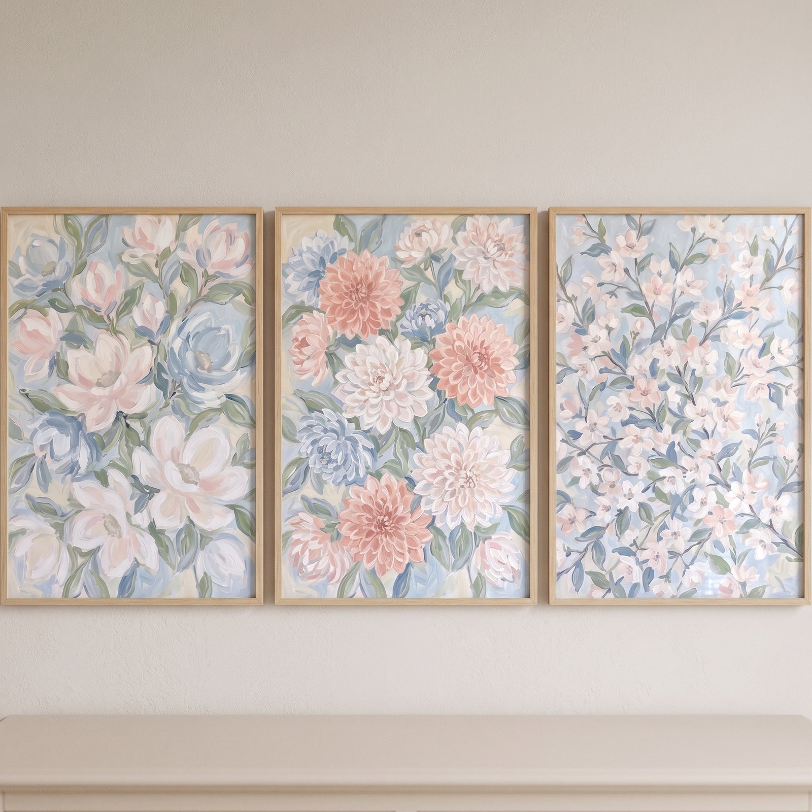 Muted sage pastel floral wall art set of 3 displays soft blue and pink blossoms in light wood frames on a neutral wall.