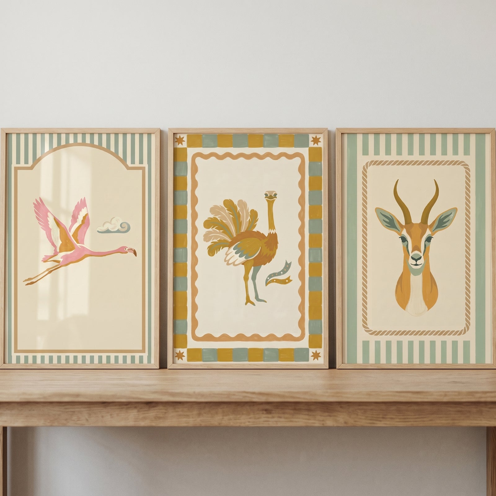 Muted sage safari animals wall art set of 3 featuring a flamingo, ostrich, and gazelle displayed on a wooden shelf.