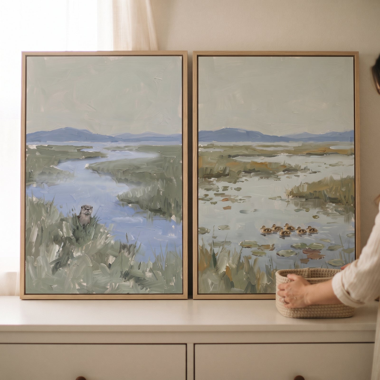 Muted sage wetland animals wall art set of 2 with an otter and ducklings in a marsh landscape above a white dresser.