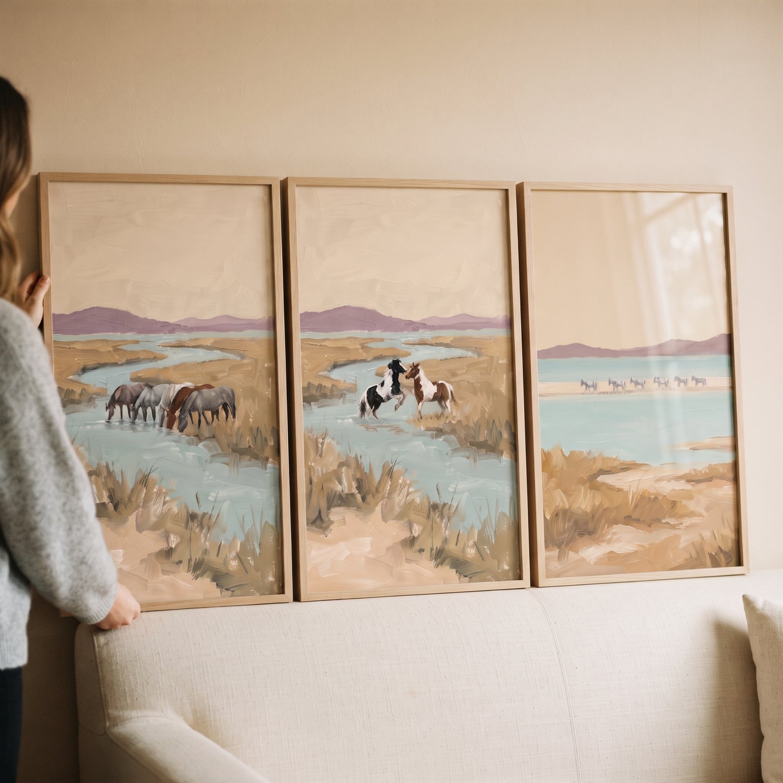 Muted sage wetland horses wall art set of 3 featuring horses in a river landscape, displayed above a neutral sofa.