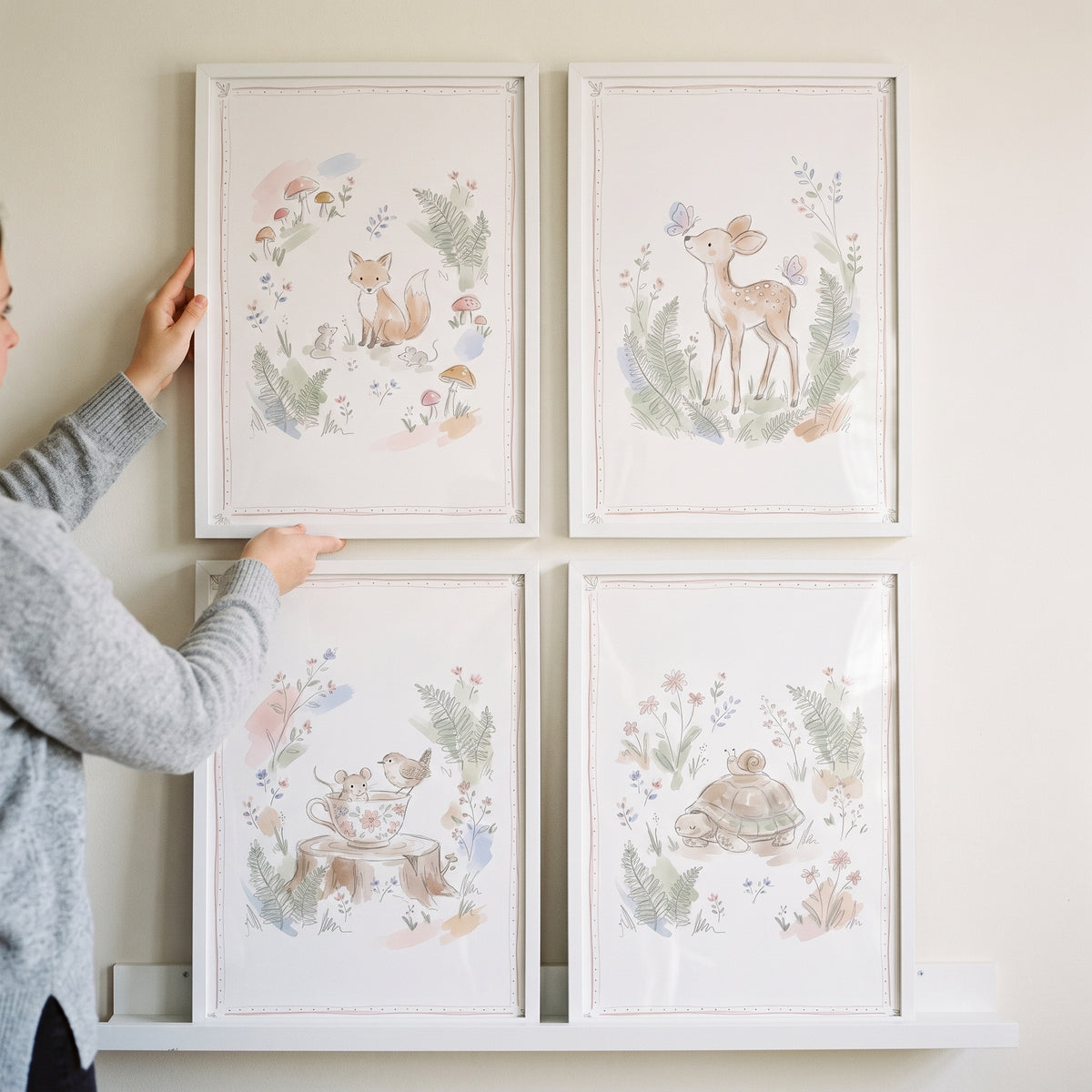 A person holds the top left piece of a muted sketch woodland animal wall art set of 4 with a fox, deer, bird, and turtle.