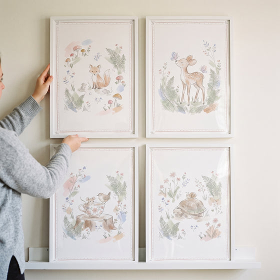 A person holds the top left piece of a muted sketch woodland animal wall art set of 4 with a fox, deer, bird, and turtle.