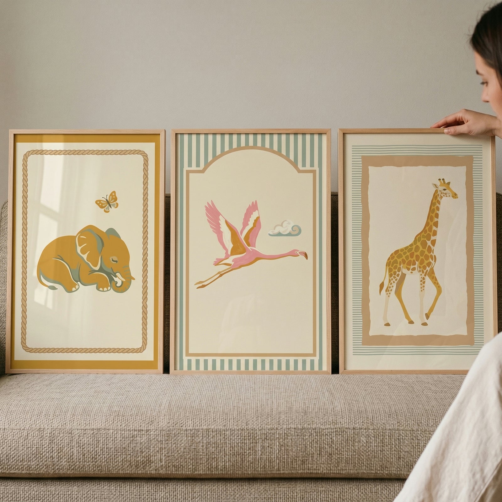 Muted terracotta safari animal wall art set of 3 featuring an elephant, flamingo, and giraffe in wooden frames on a sofa.