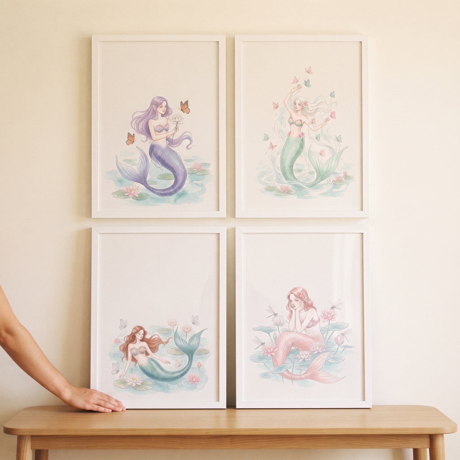 Muted tone fantasy mermaid wall art set of 4 in white frames above a wooden table as a hand touches one.