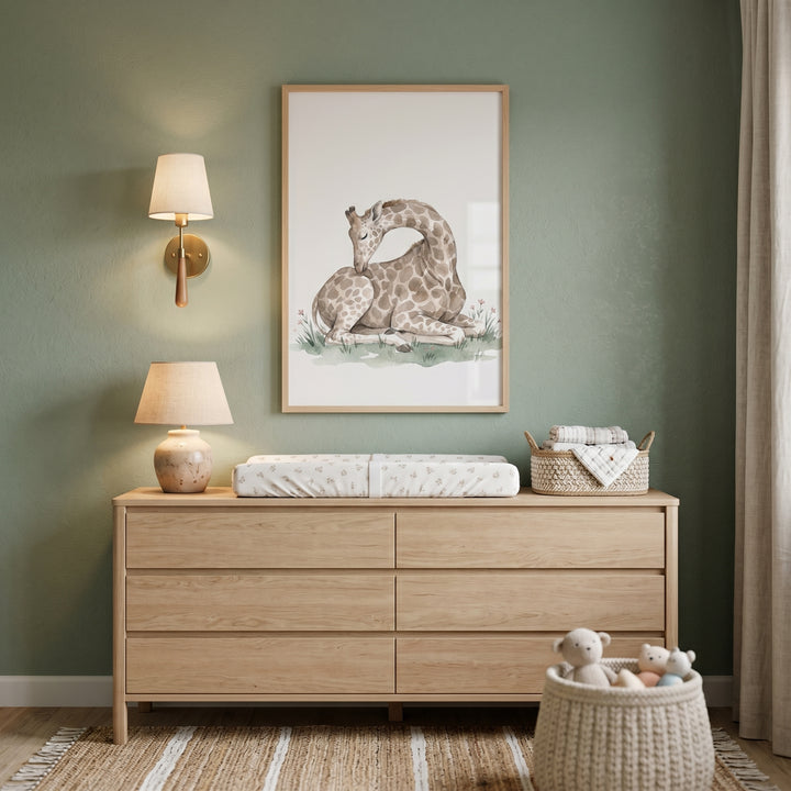 Green nursery wall with a wooden dresser, lamps, and muted tone resting giraffe artwork above a changing pad.