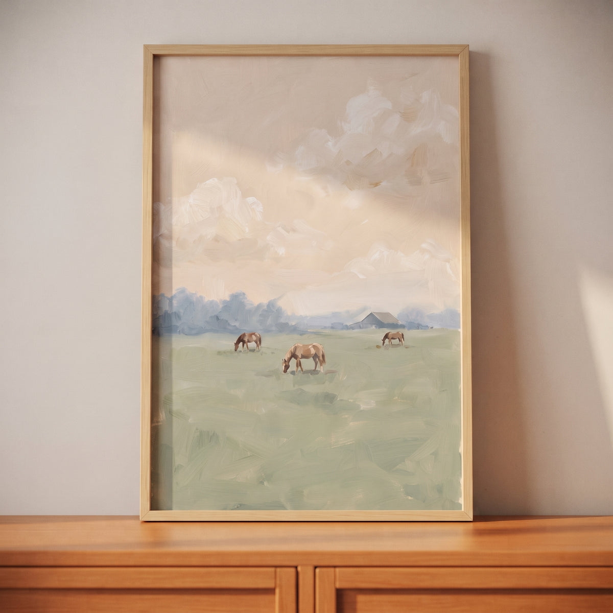 Muted tones grazing horses wall art depicts three horses in a soft green field under a vast, hazy sky in a wood frame.