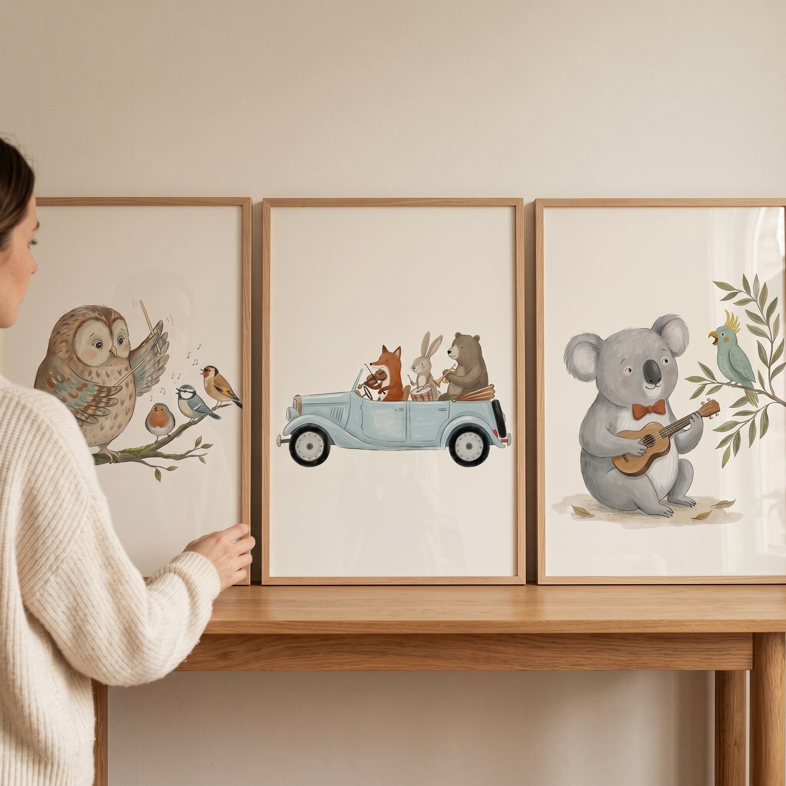 Woman adjusts a muted watercolor musical animals wall art set of 3 featuring an owl, animals in a car, and a koala.