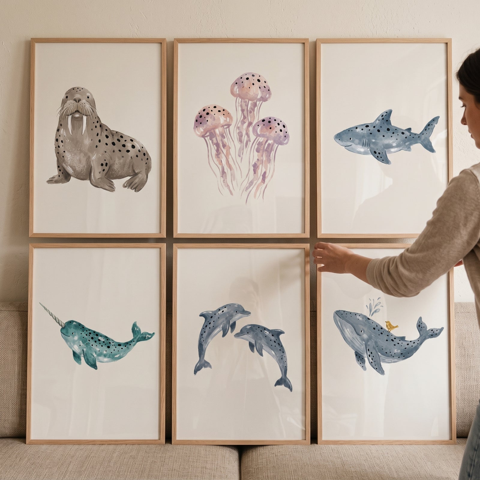 A person hangs a muted watercolor sea animal wall art set of 6 featuring a walrus, jellyfish, shark, and whale.