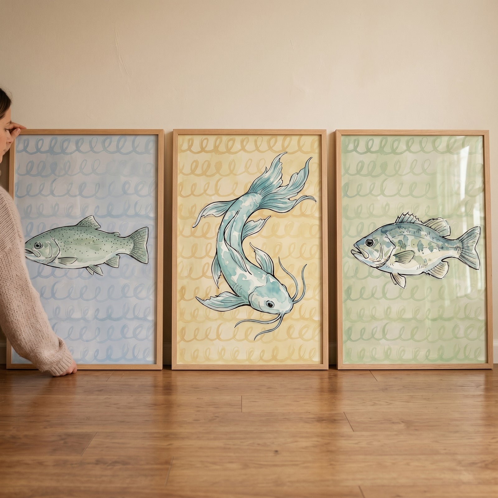 Muted watercolor sketchy fish wall art set of 3 in light wood frames held against a wall on a wooden floor.