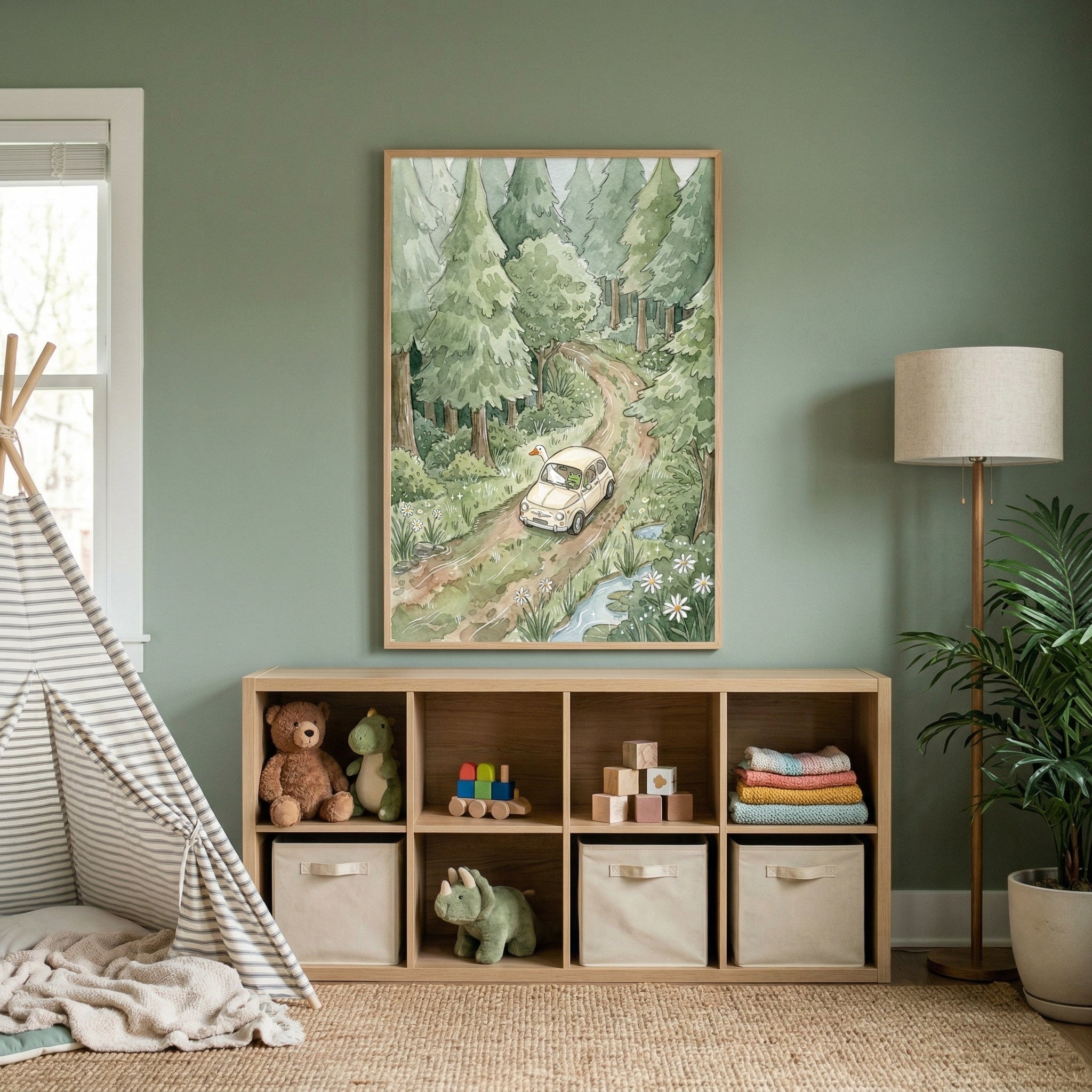 A cozy and organized nursery features a soft, muted green wall as the backdrop. Centered on the wall is a large framed vertical illustration showing a peaceful forest scene. A winding dirt road leads through a dense woods of tall, green evergreen trees. 