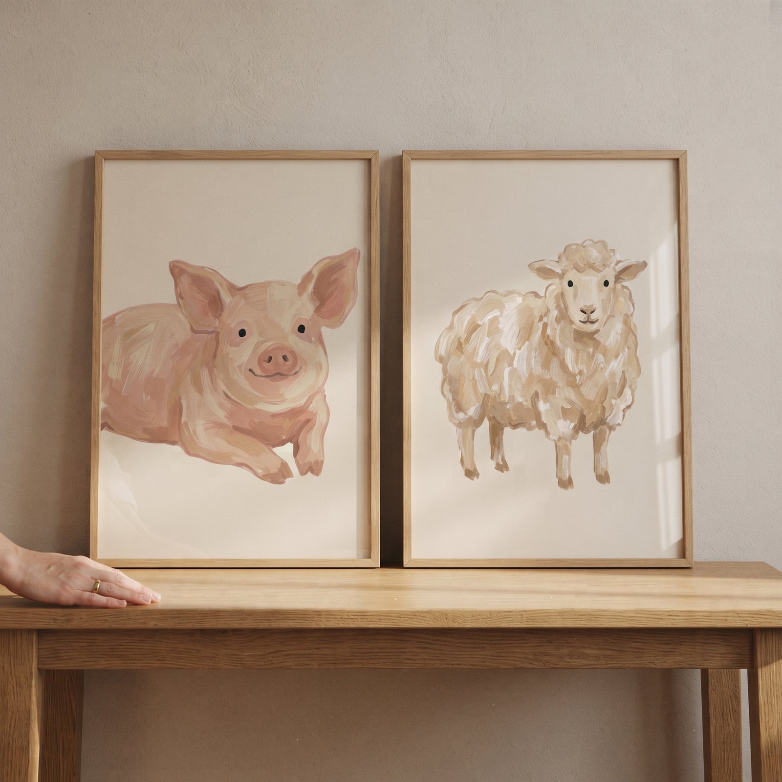 Neutral beige farm animals wall art set of 2 with a pig and sheep in wood frames on a light wood table.