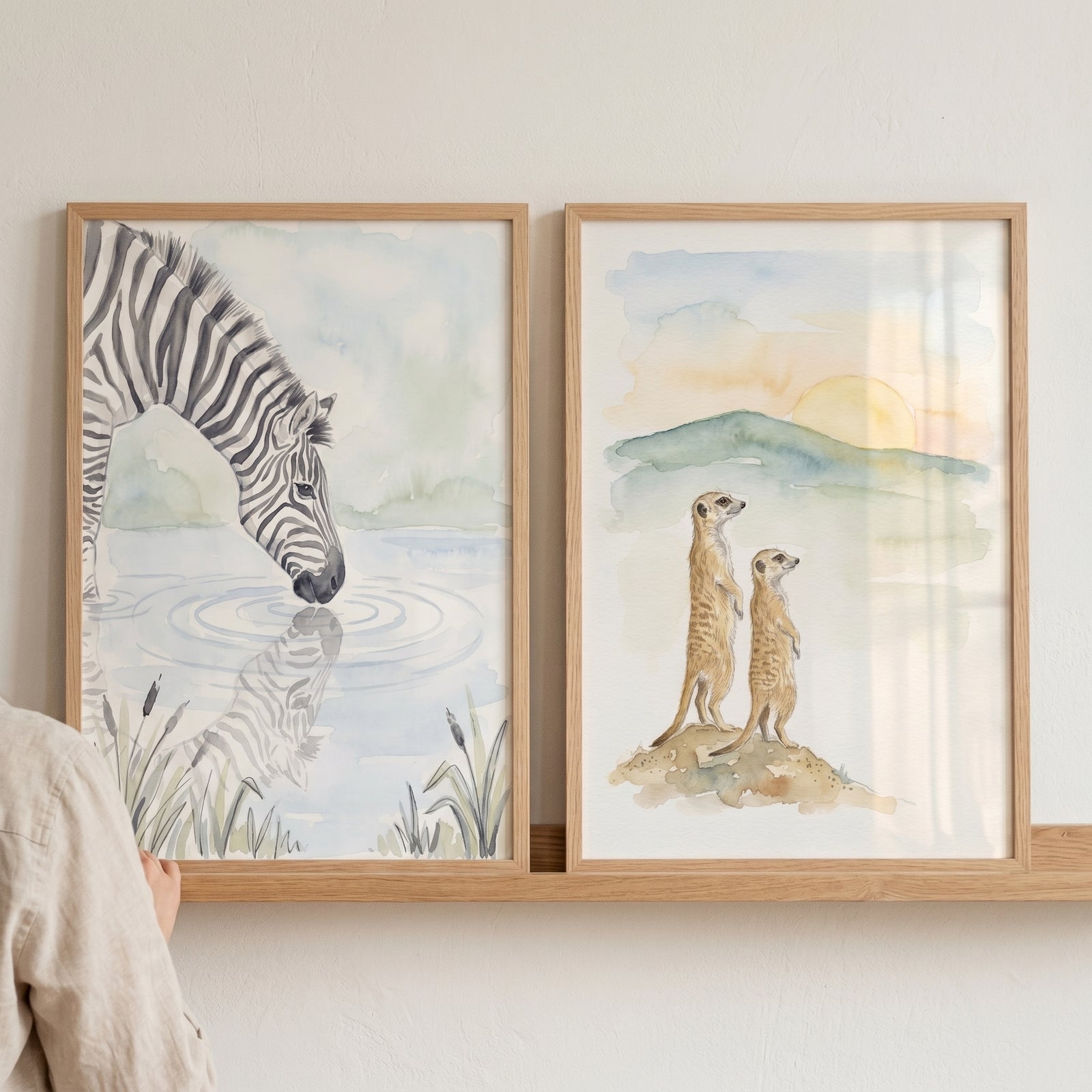 Neutral nursery safari animal wall art set of 2 featuring watercolor zebra and meerkats in light wood frames on a shelf.