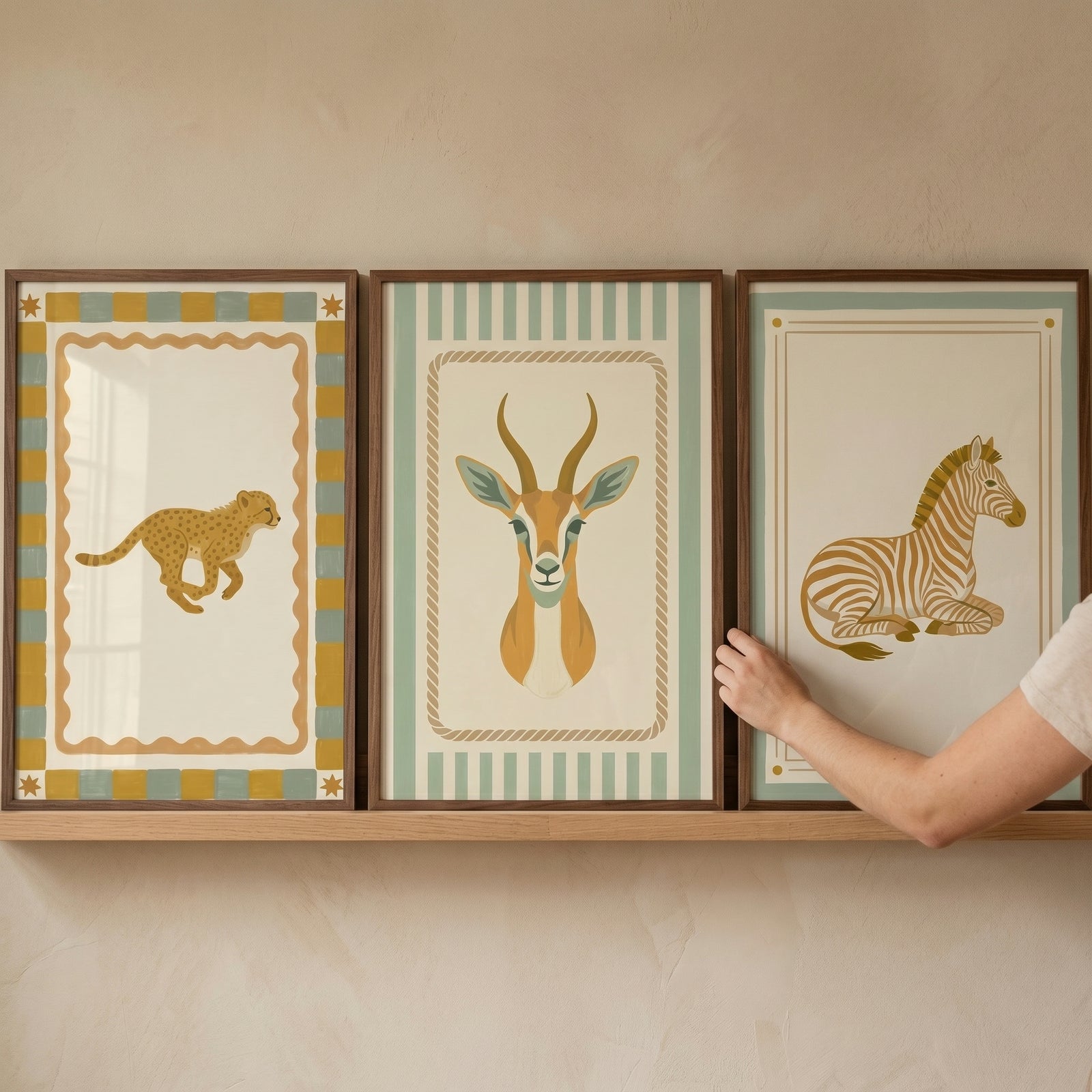 A hand touches a neutral organic safari animal wall art set of 3 featuring a cheetah, gazelle, and zebra on a shelf.