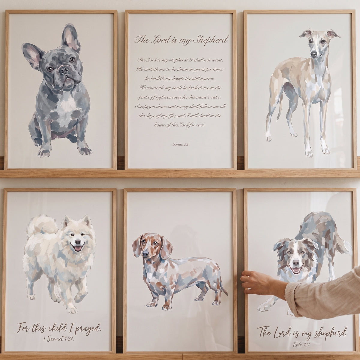 Hand adjusting a neutral religious watercolor dogs wall art set of 6 with various breeds and scripture on wooden shelves.